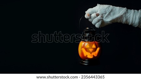 Halloween background. Zombie hand holding a lantern in the form of a pumpkin on a dark background. Halloween design. Copy space. Royalty-Free Stock Photo #2356443365