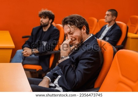 Very emotional student sitting in a lecture hall and crying with his classmates in the background Royalty-Free Stock Photo #2356473745