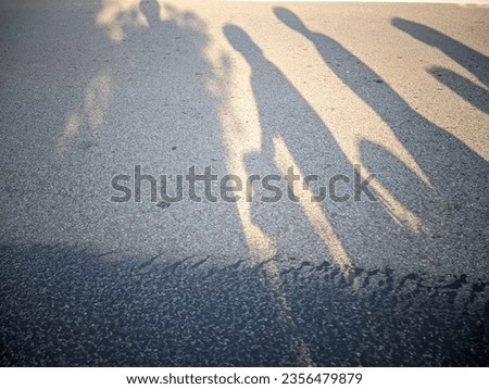 the glare of the sun forms reflections of people's shadows on the paved road surface