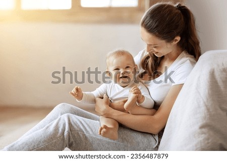 Young caucasian mom holding baby toddler, hugging carrying adorable little daughter, posing together at home, sun flare. Child care, motherhood and maternity leave concept. Empty space for text Royalty-Free Stock Photo #2356487879