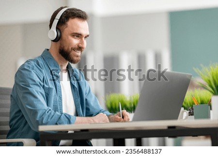 Online Education. Smiling Young Man Wearing Wireless Headphones Using Laptiop And Taking Notes, Handsome Millennial Male Watching Webinar, Attending Internet Lesson, Sitting At Desk At Office Royalty-Free Stock Photo #2356488137