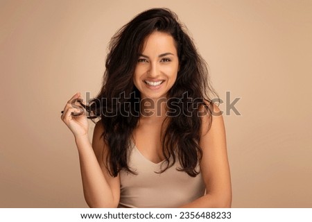 Hair styling, hair care concept. Gorgeous eastern millennial woman in beige top posing on studio background, showing her beautiful long hair after salon hair treatment and smiling at camera