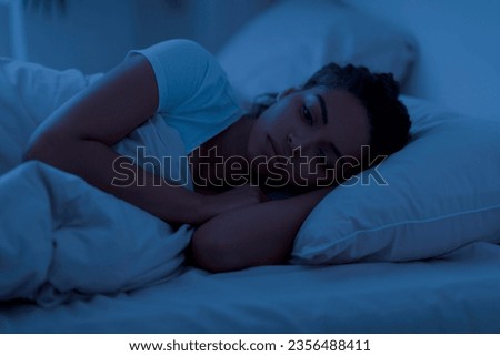 Awake sleepless upset black woman lying in bed alone at night, cant sleep, feeling lonely, suffering from depression or anxiety, experiencing difficulties with sleeping, resting in home interior Royalty-Free Stock Photo #2356488411