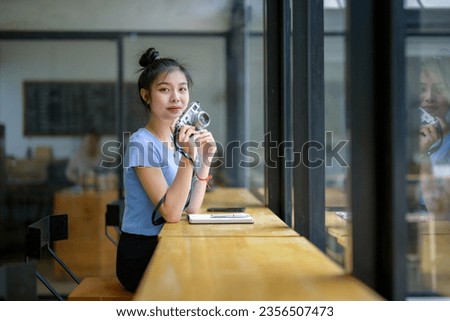 Asian woman sitting in a coffee shop use a camera to take pictures through glass windows.