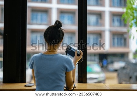 Asian woman sitting in a coffee shop use a camera to take pictures through glass windows.