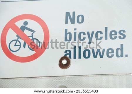 no bicycles allowed writing caption text sign with illustration picture of person on bike bicycle crossed out in circle, blue red print on white background