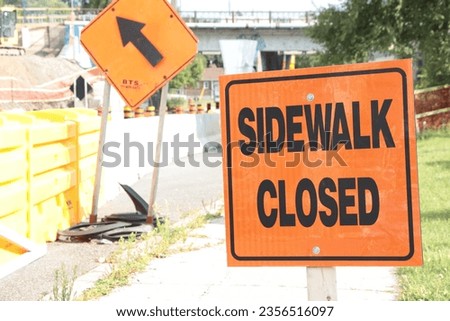orange sidewalk closed sign on sidewalk with construction and orange construction sign to left on road street, tight shot