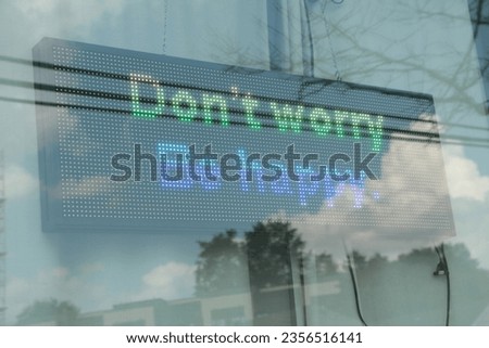 electronic electric digital rectangle horizontal sign that says dont worry be happy in green on black background inside window, close up