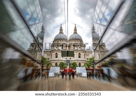 St Paul's Cathedral reflected in modern glass buildings, with red London buses and people waling by. Focus on the Cathedral with zoom blur. 