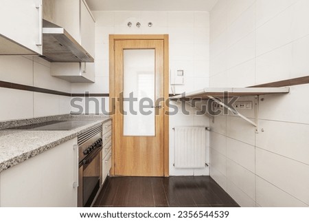 small kitchen furnished with white furniture and gray granite countertop, integrated stainless steel appliances, wooden and glass access door to the kitchen