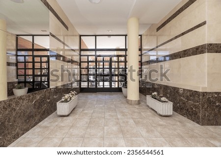 Access portal to a residential building with white flower pots, a large black metal gate, walls covered in marble and mirrors Royalty-Free Stock Photo #2356544561