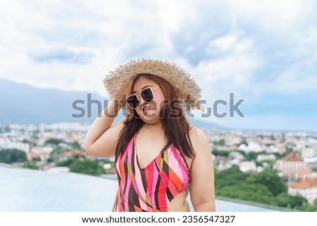 Overweight young asian woman wearing orange swimsuit and straw beach sun hat relaxing in pool Happy plus size woman cheery funny Vacation Traveling in summer