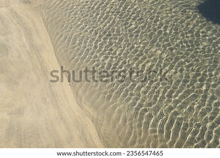 Sand, water and wind meet in this photo with ripples casting shapes and shadows on the waters edge. Taken on an Asahi Pentax camera on the beaches of Cornwall, UK. Royalty-Free Stock Photo #2356547465