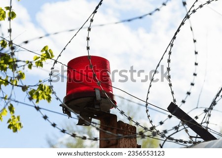 Protected area. A fence with barbed wire and a red flasher against a sky with clouds.