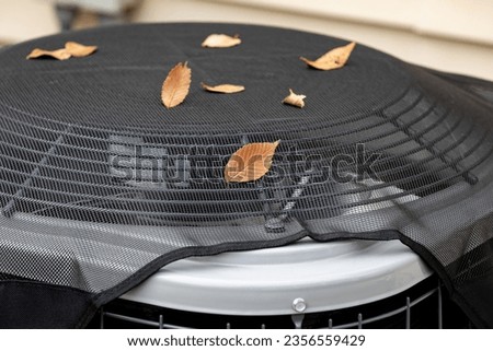House air conditioning unit with protective mesh cover during fall season. Concept of home air conditioning, hvac, repair, service, winterize and maintenance. Royalty-Free Stock Photo #2356559429