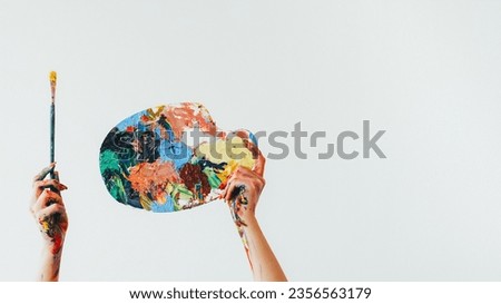 Painter equipment. Drawing tools. Woman artist hands holding colorful messy palette and paintbrush isolated on white empty space background. Royalty-Free Stock Photo #2356563179