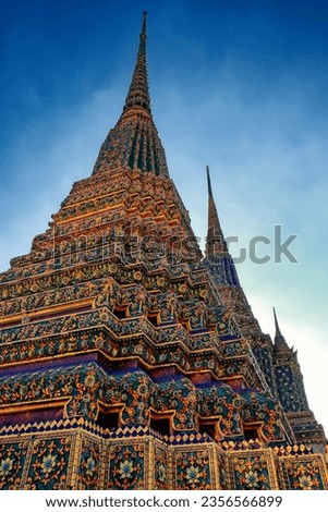 The picture presents ornate temple spires in Thailand, ornamented with colorful tiles and patterns, shining in the warm light of the sun.