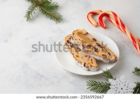 Christmas sweets, slices of stollen with marzipan and dried fruits on a white plate on a light concrete background in Christmas style. Merry Christmas concept, sweets from all over the world Royalty-Free Stock Photo #2356592667
