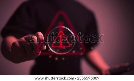 Hand holding magnifier glass with red triangle caution warning sign for focus notification error and maintenance concept.