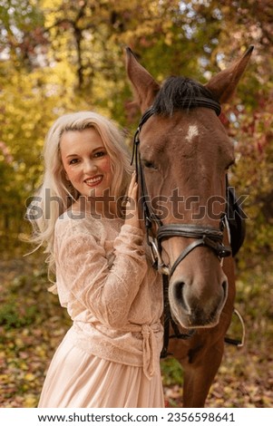 A woman in dress stands next to a horse. Horseback riding in the autumn forest