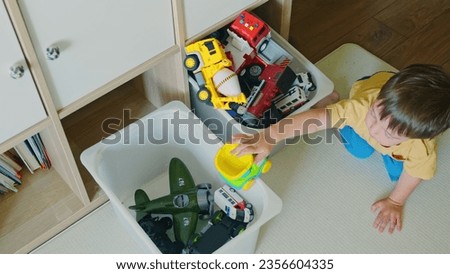 Baby boy is putting the toys back in the box after playing. Kid toddler boy aged two years Royalty-Free Stock Photo #2356604335