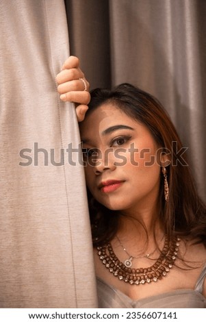 a beautiful Asian woman holding the curtains while posing for photos in a studio during the day