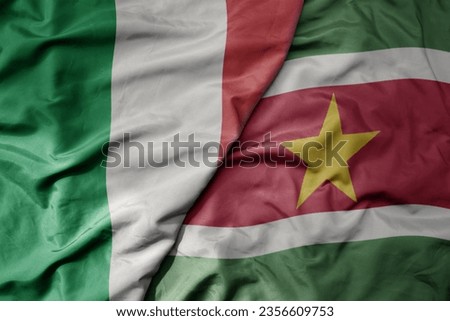 big waving national colorful flag of italy and national flag of suriname . macro
