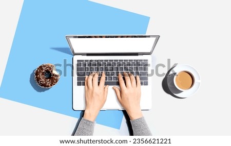 Person using a laptop computer with a donut and a cup of coffee - Flat lay