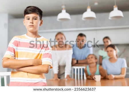 Sullen boy child crossed arms crossed over chest and is standing with back to parents and sisters. Large family is outraged by negligent behavior of teenage son Royalty-Free Stock Photo #2356623637