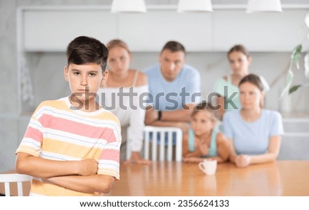 Sullen boy child crossed arms crossed over chest and is standing with back to parents and sisters. Large family is outraged by negligent behavior of teenage son Royalty-Free Stock Photo #2356624133