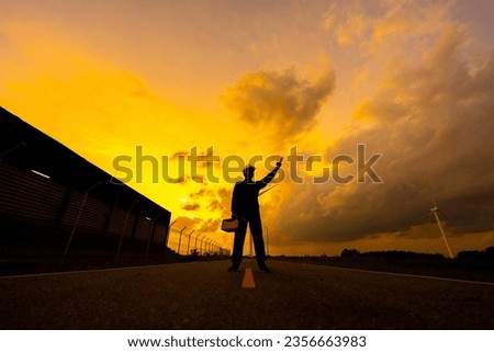 Male engineer wearing a vest and helmet Hold the tool crate and point it to the destination. Nearby there is a wind turbine. Standing near an industrial factory In the golden twilight sky scene