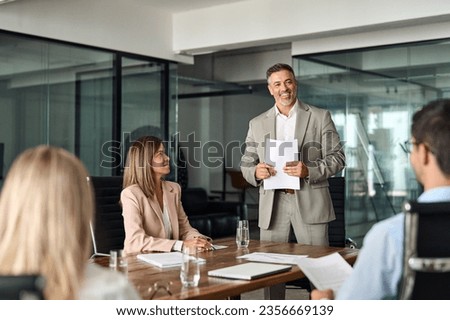 Happy mature older Latin business man team manager CEO executive leading group corporate meeting in board room. Diverse business team people company staff working together at office table. Royalty-Free Stock Photo #2356669139