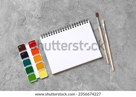 Notepad and paints on gray background, top view