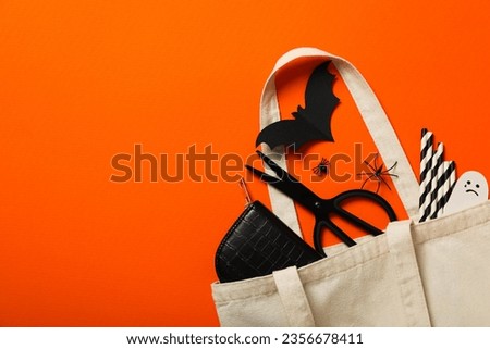 Scissors, case, paper ghost and bat in cotton bag on orange background, space for text