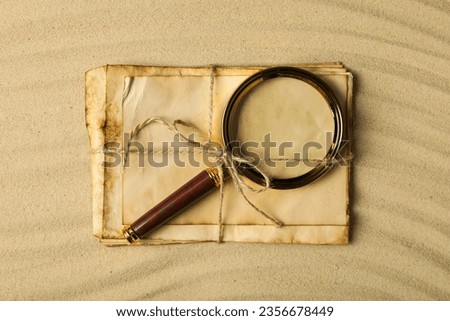 Columbus Day. A magnifying glass with a stack of letters on the sand