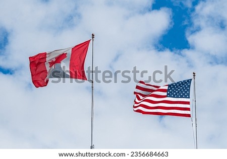 Flag of Canada and the USA against the background of the blue sky with white clouds. America and Canada national flag cloth fabric waving on the sky. American and Canadian flags together. Top view.