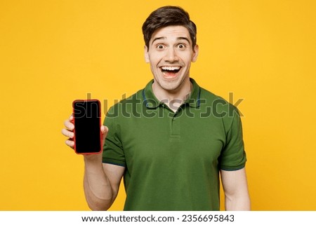 Young smiling cheerful caucasian happy man wears green t-shirt casual clothes hold in hand use mobile cell phone with blank screen workspace area isolated on plain yellow background. Lifestyle concept