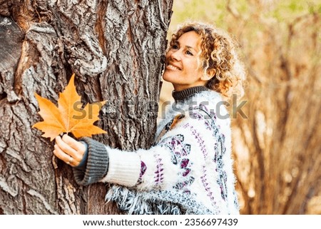 One happy adult woman hug a tree and smile in autumn season outdoor leisure activity. Natural lifestyle and love nature concept people. Yellow color woods and trees in background. Female enjoying park Royalty-Free Stock Photo #2356697439