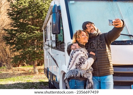 Happy couple of vanlife camper van tourist taking selfie picture with smartphone outside the travel vehicle home. Concept of tourism with rv camping car motorhome. Alternative lifestyle people smile