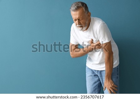 Mature man having heart attack on blue background Royalty-Free Stock Photo #2356707617