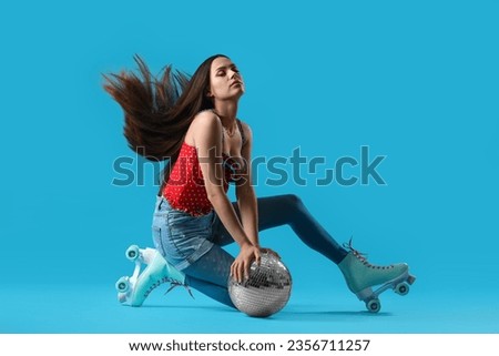Beautiful young woman in roller skates with disco ball on blue background