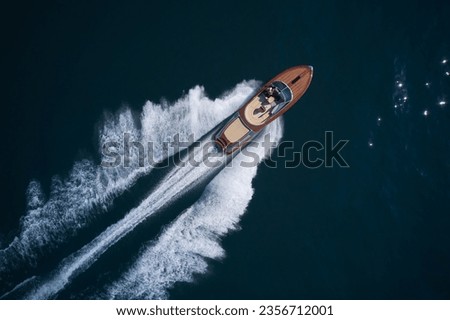Luxurious wooden boat fast movement on dark water. Classic Italian wooden boat fast moving aerial view. Top view of a wooden powerful motor boat. Large expensive varnished wooden boat top view Royalty-Free Stock Photo #2356712001