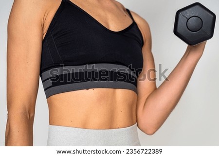 Sporty woman doing exercises with metal dumbbells training against the background of a plain white wall. Photo of a muscular woman in sportswear on a white background. Strength and motivation. muscles
