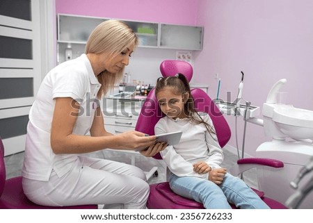 woman dentist shows a cartoon to a girl on a tablet before examining her oral cavity. dentistry for children. review
