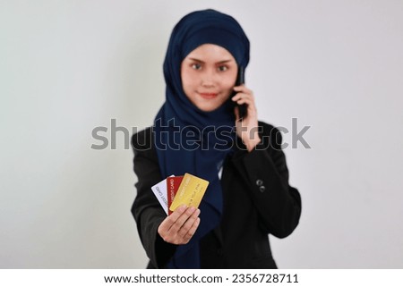 Happy smart asian business woman hands in muslim dress standing while using smart mobile phone and smiling with credit card in studio. Isolated white background portrait with beautiful face in hijab.