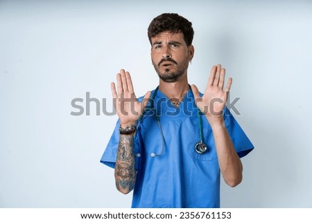 young caucasian doctor man wearing blue medical uniform Moving away hands palms showing refusal and denial with afraid and disgusting expression. Stop and forbidden. Royalty-Free Stock Photo #2356761153