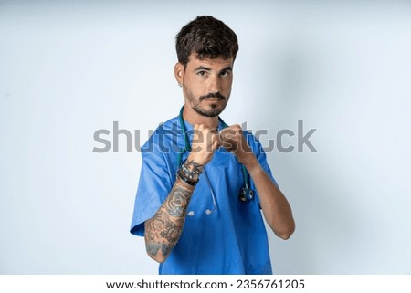 young caucasian doctor man wearing blue medical uniform Ready to fight with fist defense gesture, angry and upset face, afraid of problem.