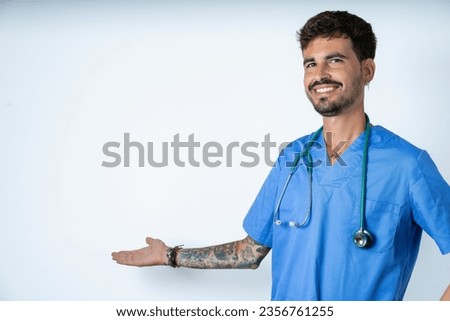 young caucasian doctor man wearing blue medical uniform feeling happy and cheerful, smiling and welcoming you, inviting you in with a friendly gesture