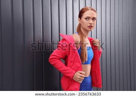 Beautiful woman in gym clothes posing near dark grey wall on street