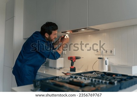 Professional male worker in uniform repairing modern cooker hood in kitchen Royalty-Free Stock Photo #2356769767